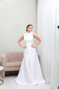 Indoor full length image of bride in white classic dress and bridal tiara, minimalist home interior