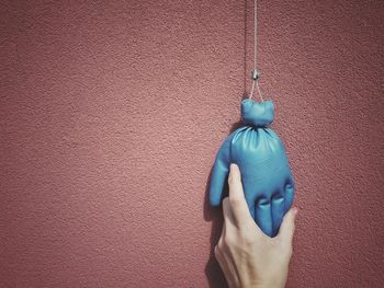 Close-up of woman holding hanging blue glove against brown wall