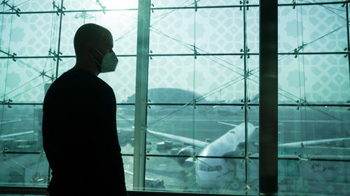 Rear view of silhouette man standing by glass window