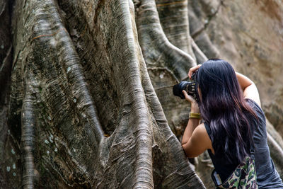 Rear view of woman photographing tree trunk with camera