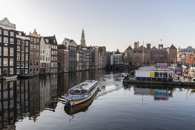 Boats moored on river by buildings in city against sky