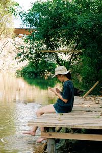 Man sitting on seat by lake against trees