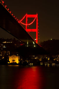 Illuminated bridge over river against sky at night