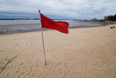 Red flag on beach against sky