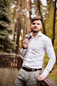 Young man looking away while standing by railing against trees in forest