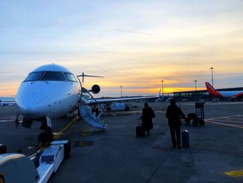 People on airport runway against sky during sunset