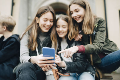 Young woman using smart phone while sitting on laptop