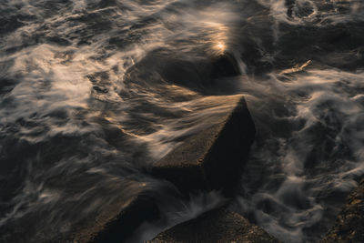 Full frame shot of waves splashing on rocks in sea during sunset