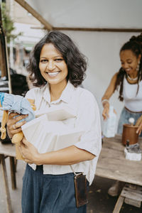 Portrait of smiling woman with books and stuffed toy at flea market