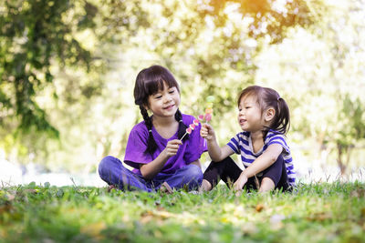 Cute sisters holding lollipop sitting on grass at park