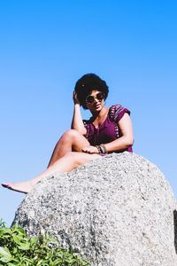 Low angle view of woman standing on rock against clear blue sky