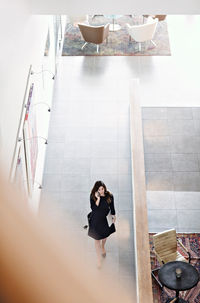 High angle view o businesswoman talking on smart phone while walking in corridor by cafeteria