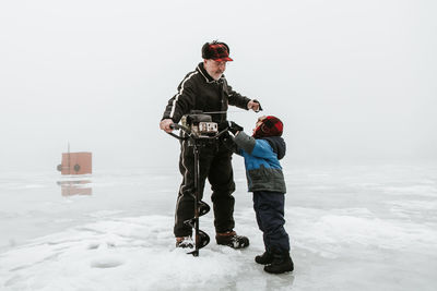 Grandfather and grandson making hole in ice rink