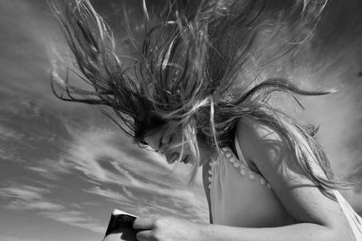 Woman with tousled hair holding book against sky