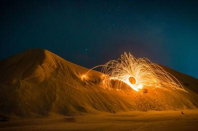 Firework display on desert against sky at night