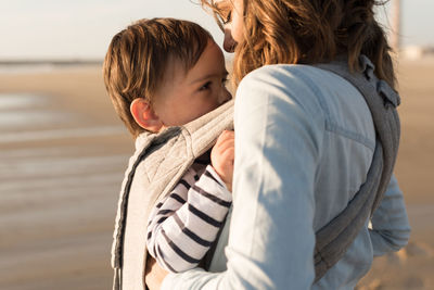 Mother carrying son while standing at beach