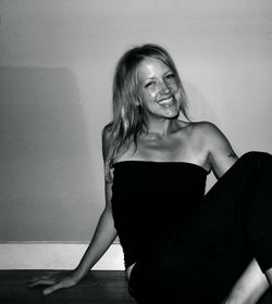 Portrait of smiling young woman sitting by wall at home