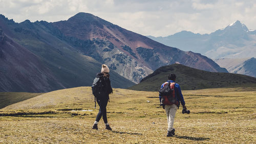 Rear view of hikers walking on field against mountains