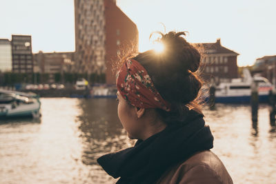 Side view of mid adult woman looking at river in city during sunset