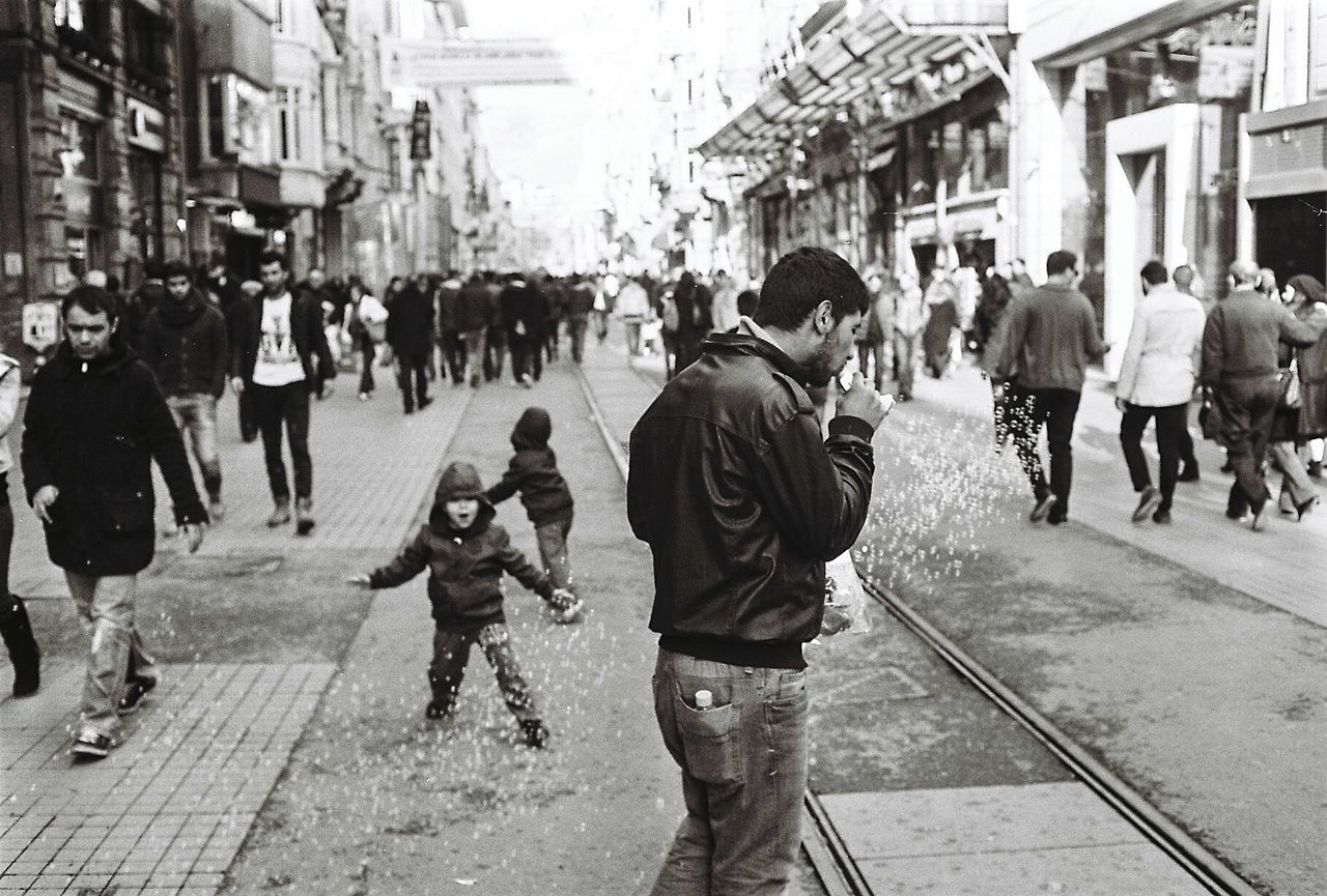 walking, building exterior, men, large group of people, street, person, city, architecture, city life, built structure, lifestyles, city street, rear view, transportation, leisure activity, full length, road, casual clothing, on the move