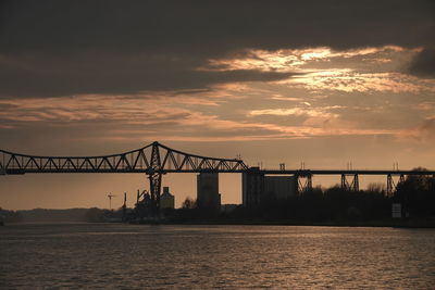 Silhouette bridge over sea against sky during sunset