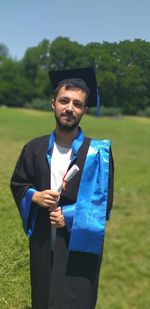 Portrait of young man wearing graduation gown while standing on land