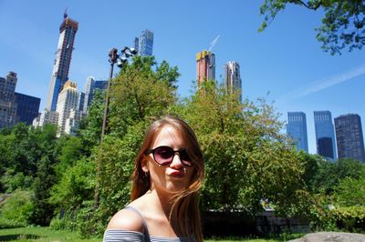 Young woman wearing sunglasses against building in city during sunny day