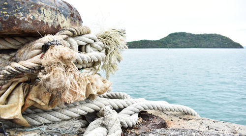 Close-up of rope tied on rock by sea against sky