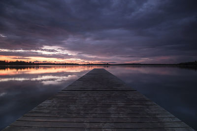 Jetty over lake against cloudy sky during sunset