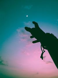 Low angle view of silhouette hand holding leaf against sky at sunset