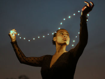 Woman looking at illuminated camera against sky