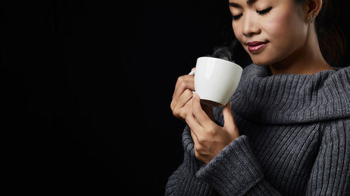 Young woman drinking coffee cup against black background