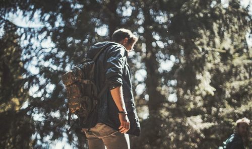 Low angle view of man with backpack standing in forest