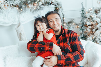 Portrait of smiling father with daughter sitting on sofa at home