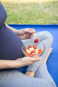 Midsection of pregnant woman eating fruits in bowl