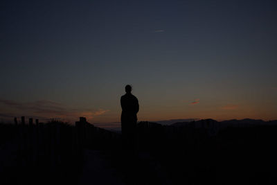 Silhouette man standing on landscape against clear sky at sunset