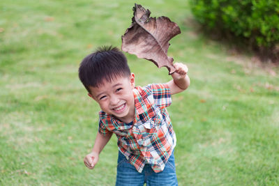 Portrait of boy holding dry leaf while standing on field