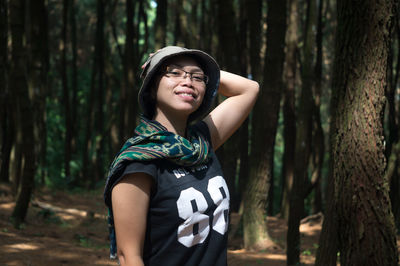 Portrait of woman standing by tree trunk in forest