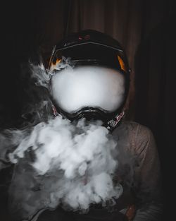 Close-up of man wearing helmet smoking against black background