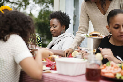 Family and friends eating food on picnic table at backyard