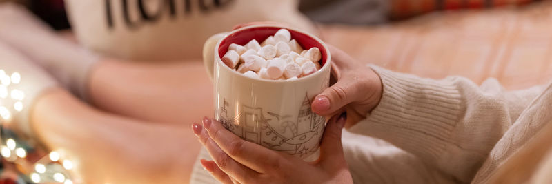 Cup of hot chocolate drink with marshmallows in female holding hands of woman in knitted sweater 