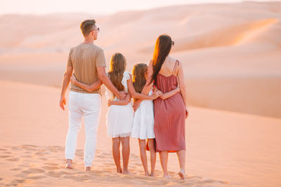 Rear view of parents with daughters standing at desert during sunset