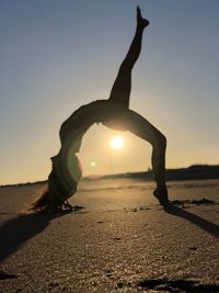 Woman exercising on road against sky during sunset