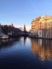 Buildings by canal in city against clear sky