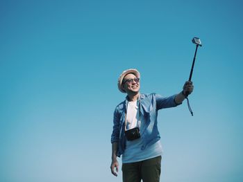 Low angle view of happy man taking selfie with monopod against clear blue sky