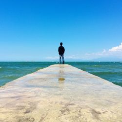 Rear view of man standing on beach against clear blue sky