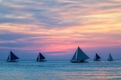 Sailboats sailing in sea against sky during sunset