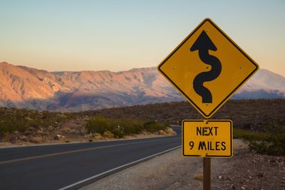 Information sign on road by mountains against sky