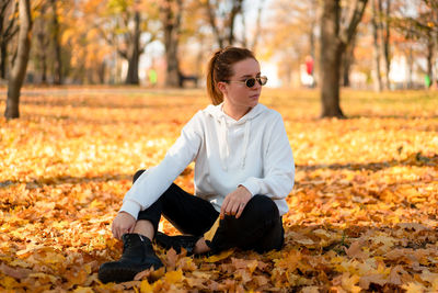 Full length of woman sitting on autumn leaf at park