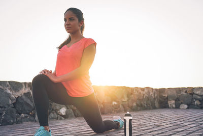 Young woman exercising on promenade against sky during sunset